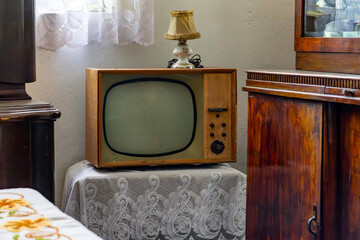 Vintage CRT TV from the communist era on a lace doily, next to a retro lamp and mid-century wooden furniture – classic 1960s–70s interior.