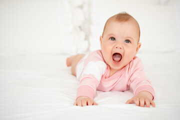 A baby girl smiles or laughs lying on her tummy, a cute and smiling little baby in a pink bodysuit...