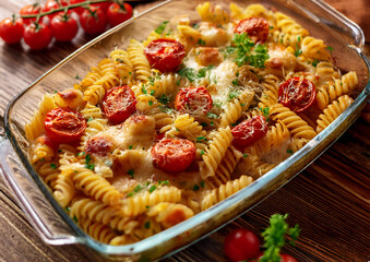 Zapiekany makaron fusilli z warzywami i roztopionym serem w przeźroczystym naczyniu żaroodpornym, przybrane świeżą pietruszką na wierzchu.