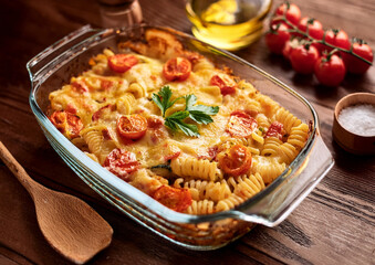 Zapiekany makaron fusilli z warzywami i roztopionym serem w przeźroczystym naczyniu żaroodpornym, przybrane świeżą pietruszką na wierzchu.