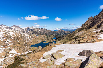 Snowy mountain landscape in the Pyrenees, with rocky peaks, blue sky and alpine lakes along the...