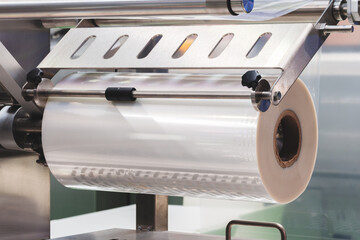 A machine with a roll of polyethylene plastic wrapping film on it. The machine is in a factory....