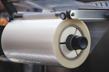 A machine with a roll of polyethylene plastic wrapping film on it. The machine is in a factory....