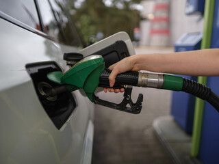 Close up of a person refueling a car at a gas station using a green fuel nozzle. Concept of transportation, energy, travel readiness, routine, technology, and modern lifestyle.