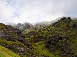 Rugged, green landscape viewed along the Carrauntoohill walkway. Mist and clouds obscure the higher...