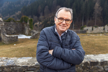 Elderly caucasian male smiling outdoors in winter jacket at scenic mountain ruins