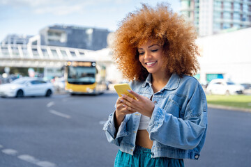 Latin student girl using cellphone phone standing on city street traffic in background. Smiling...