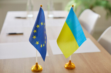 Flags of European Union and Ukraine standing on meeting table during political summit. Peaceful...