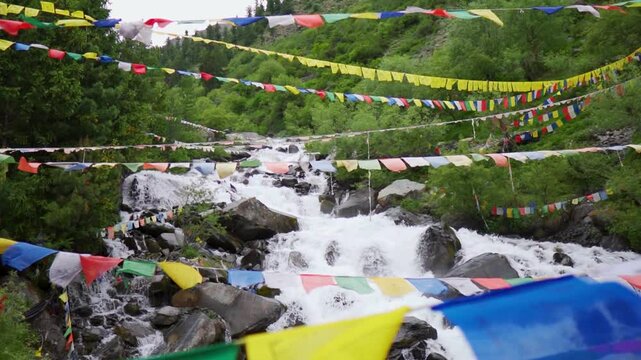 Slow motion shot of a water stream in the Himalayan mountains with prayer flags waving above it as seen near Triloknath village in Pattan valley, Himachal Pradesh, India. Scenic view of waterfall.