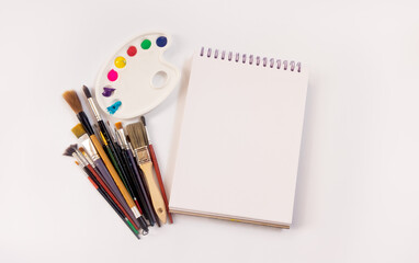 Composición de pinceles, libreta y paleta de pinturas sobre fondo blanco