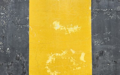A dark grey cement wall painted yellow in the middle. The old wall has peeling paint and stains and...