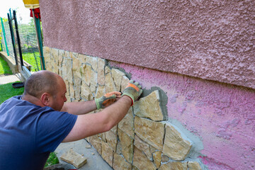 A man in gloves meticulously lays decorative stone on a wall, creating a durable and aesthetically...