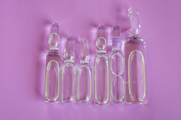 A row of transparent glass ampoules of various sizes, filled with liquid, is arranged on a delicate...