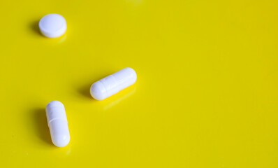 Several white pills of different shapes – one round and two capsules – are arranged on a bright...