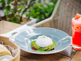 Buratta cheese salad with avocado cream base in blue rustic plate in restaurant or cafe table. Burratina fresh healthy meal food snack diet on wooden table in summer sunny day outdoor, copy space