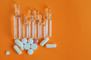 A collection of clear ampoules and colorful capsules and pills, arranged on a monochromatic orange...