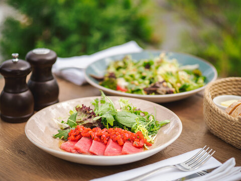 Tuna fillet with strawberry concasse and green salad with fresh herbs and teriyaki sauce in rustic plate. Delicious food in summer sunny day outdoor of restaurant or cafe terrace