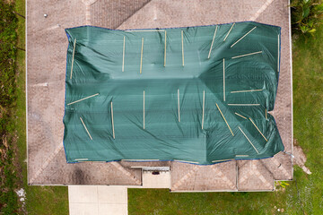 Hurricane damaged house rooftop covered with protective plastic tarp against rain water leaking...