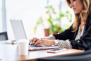 Confident middle aged businesswoman sitting at desk and using a computer laptop in her office