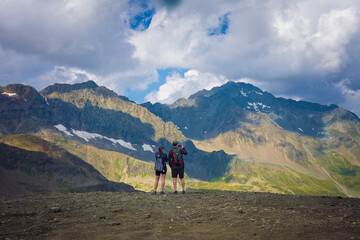 Couple of young hikers, back unidentified; admiring the Swiss Alps from the Glacier of the Stubai valley