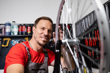 Professional serviceman balancing bicycle wheel in workshop.