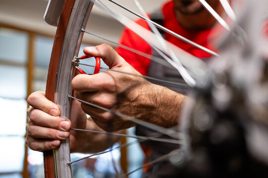 Experienced serviceman adjusting bicycle wheel spokes in workshop.