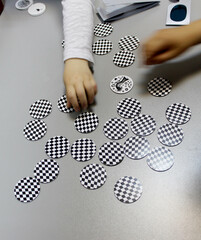 Board game, a visual perception exercise for visual therapy. Pieces of different colors and shapes are placed on the board according to rules. Children's hands playing a board game with pieces.