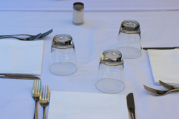Minimalist dining table setting with white tablecloth, cutlery, glassware, ready for guests