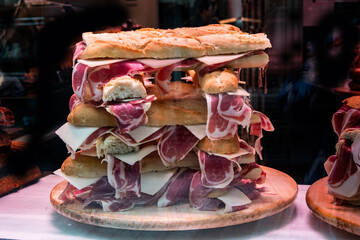 Spanish ham and chees sandwich with baguette bread, stacked in a display case from a shop on a street