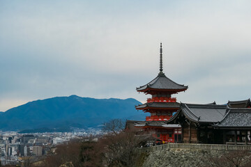 Fototapeta premium The historic red pagoda and halls of Kiyomizu-dera Temple are perched on a hill, offering a breathtaking panoramic view of the Kyoto cityscape below and the majestic mountains on the horizon in Japan.