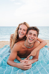 A cheerful couple is lying on a beach towel, laughing and embracing each other joyfully under the...