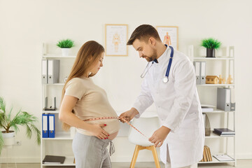 Fototapeta premium Young pregnant woman belly measuring during visiting doctor in clinic, male medical gynecologist consulting expectant mother, prenatal, healthy pregnancy, prenatal testing, professional antenatal care