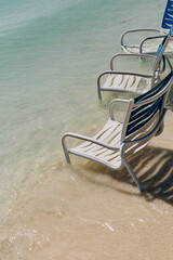 Obraz premium Beach chairs partially submerged in clear water along a sandy shore under bright sunlight