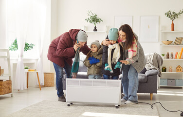 Cold parents and children dressed in warm clothes standing by electric heater, trying to get warm....