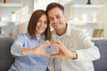 Couple in love making finger heart frame, loving portrait, happy man and woman in love, having fun, posing, smiling, enjoying being together, celebrating holiday together, sitting close at sofa 
