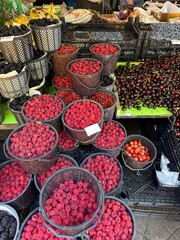 Various types of fresh berries and cherries are displayed in black plastic baskets at an outdoor...