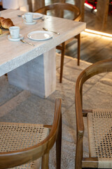 Petit déjeuner appétissant servi sur une élégante table en bois avec chaises en cannage, dans une salle lumineuse et chaleureuse. Zoom sur le mobilier.