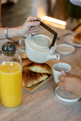 Petit déjeuner appétissant servi sur une élégante table en bois avec chaises en cannage, dans une salle lumineuse et chaleureuse. Zoom sur une personne qui sert.