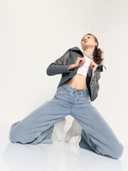 A stylish woman in trendy jeans and a jacket poses sitting on the floor
