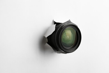 Hidden camera lens through torn hole in white paper
