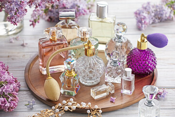 Bottles of perfumes, accessories and lilac flowers on white wooden table