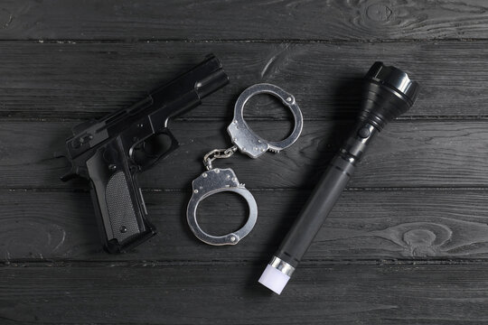 Gun, handcuffs and flashlight on black wooden table, flat lay. Police equipment