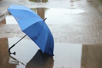 Blue umbrella on wet asphalt outdoors, space for text