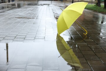 Yellow umbrella on wet asphalt outdoors, space for text