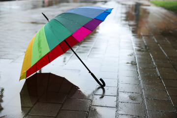 Colorful umbrella on wet asphalt outdoors, space for text