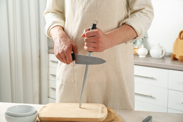 Man sharpening knife with sharpener at beige table indoors, closeup