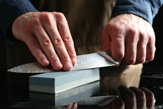 Man sharpening knife with sharpener at mirror table, closeup