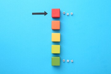 Words Min and Max, colorful cubes and arrow pointing at red one on light blue background, flat lay