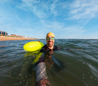 Triathlete swimming in open water with safety buoy and goggles