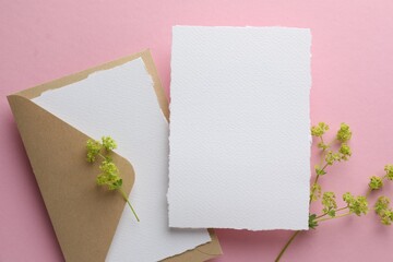 Wedding invitation cards, envelope and branches with flowers on pink background, flat lay